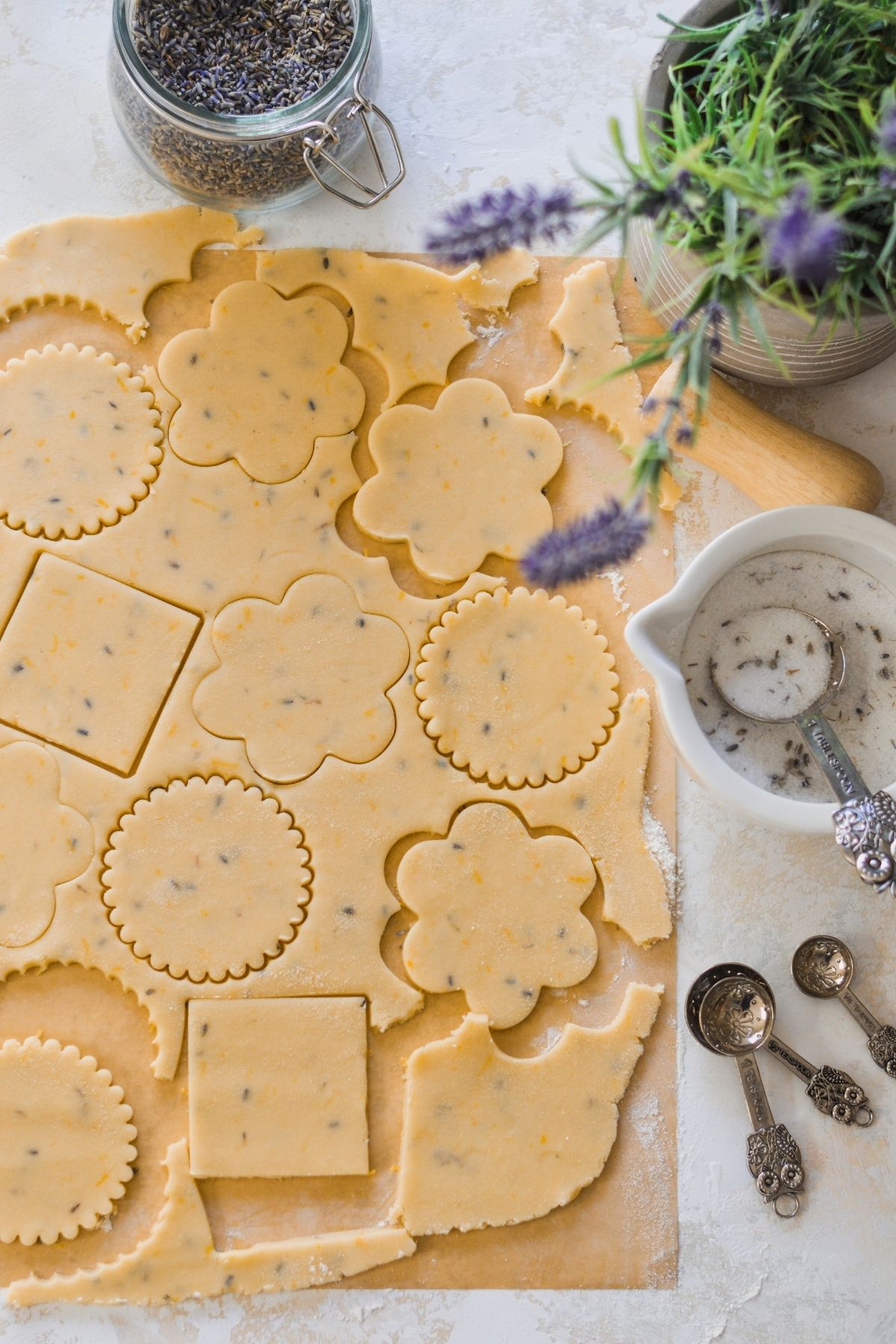 Lemon lavender cookie dough punched out with round fluted, squared and flower cookie cutters.