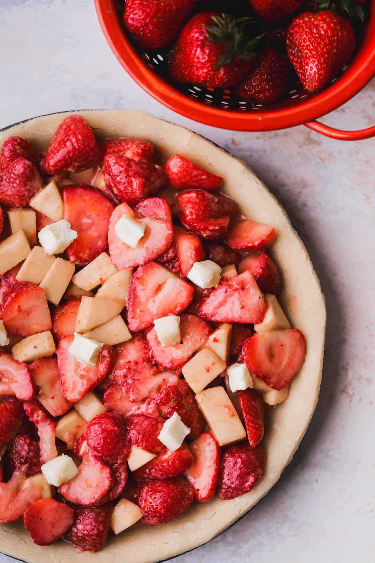 Fresh strawberry and apple mixture inside pie crust with dollops of butter on top.