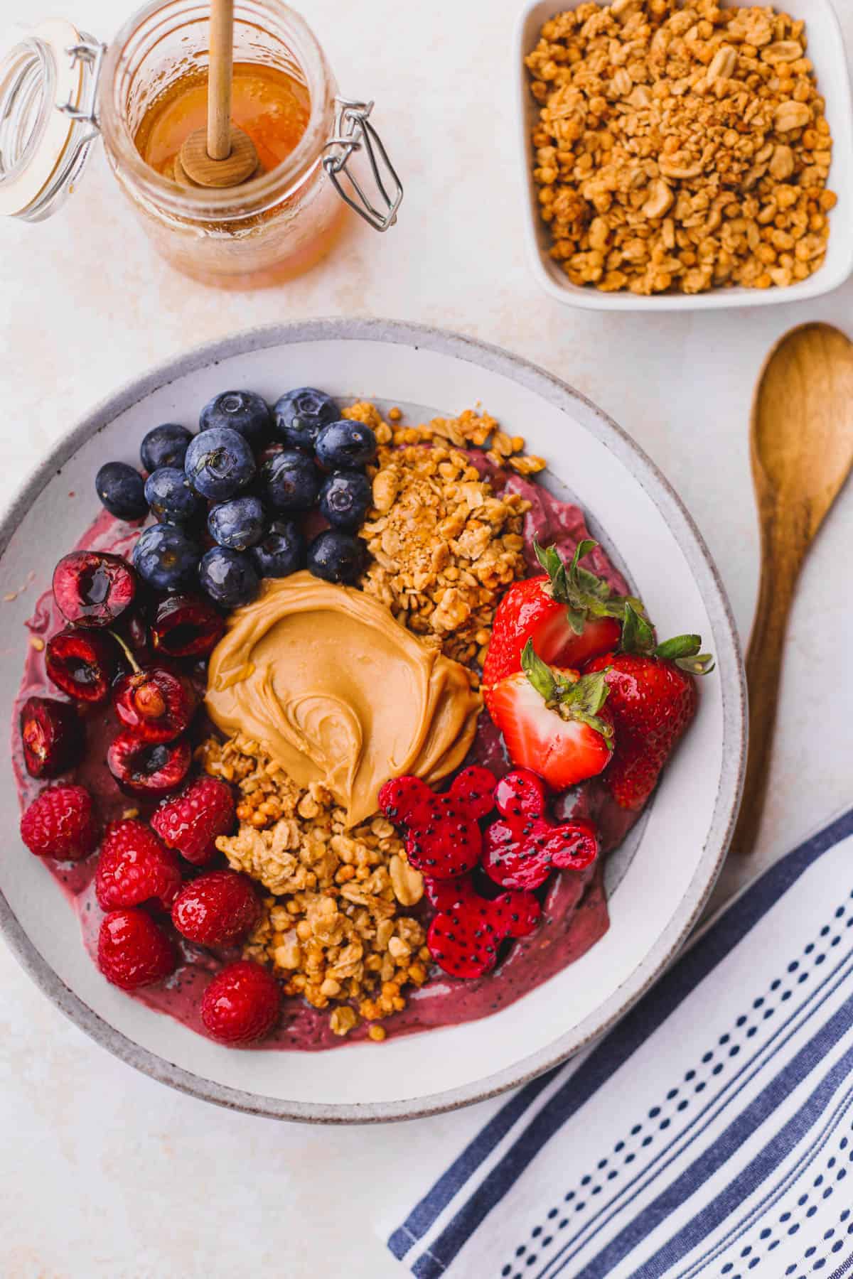 Peanut butter acai bowl is made with frozen berries, bananas and peanut butter. Topped with granola, berries, more peanut butter and honey.