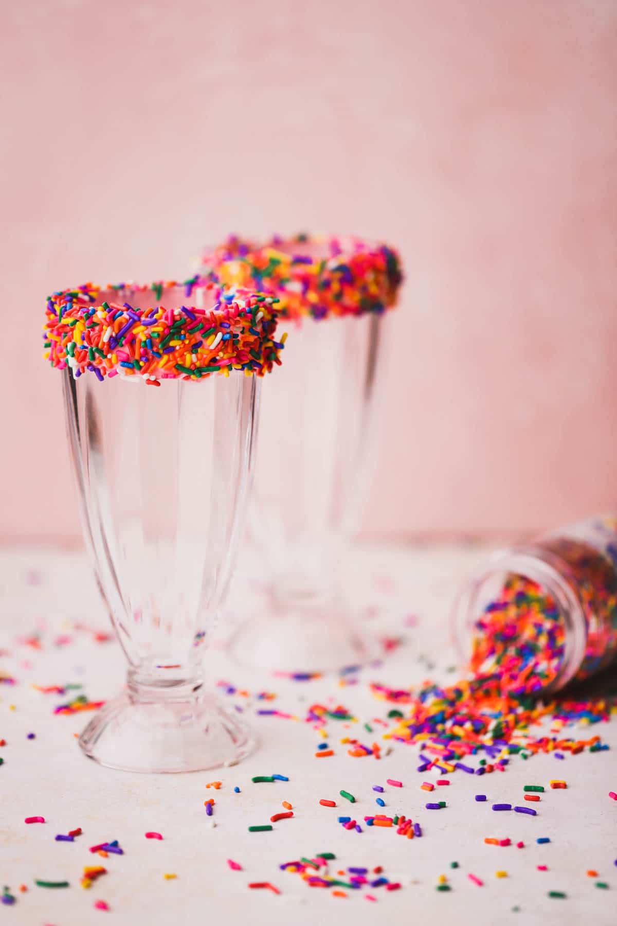 Milkshake glass rim decorated with frosting and rainbow sprinkles.