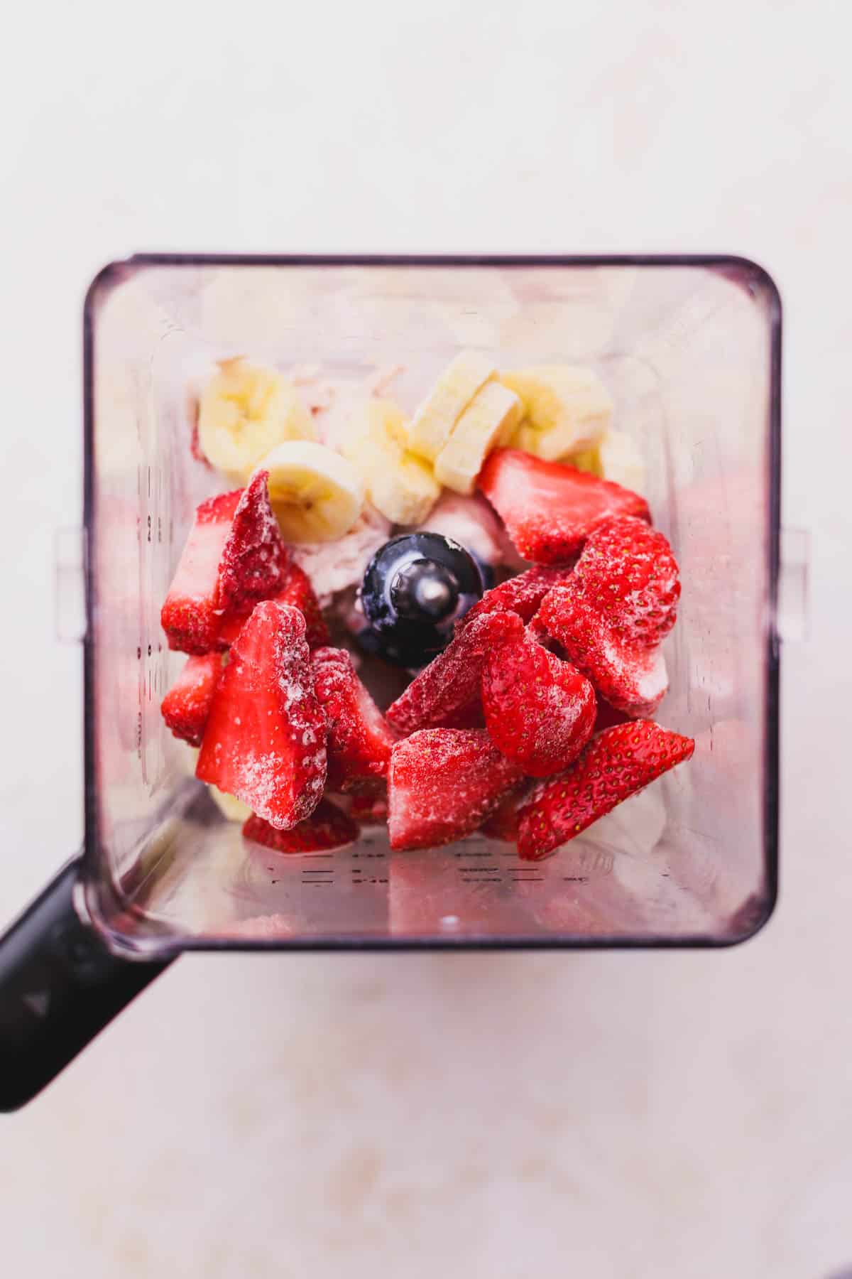 Strawberry ice cream, frozen strawberries, banana and milk inside blender.