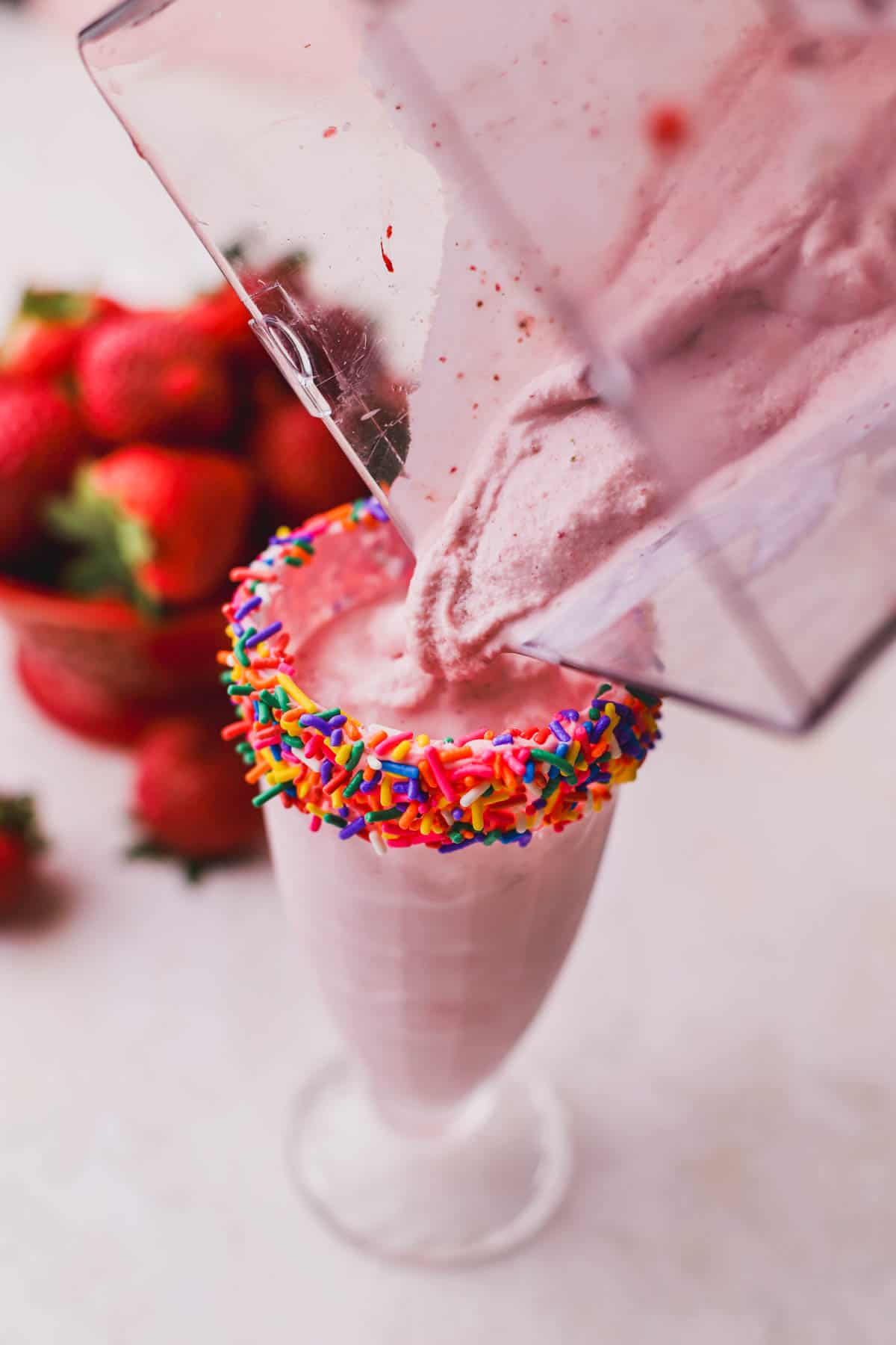 Pouring strawberry and banana milkshake inside glass.