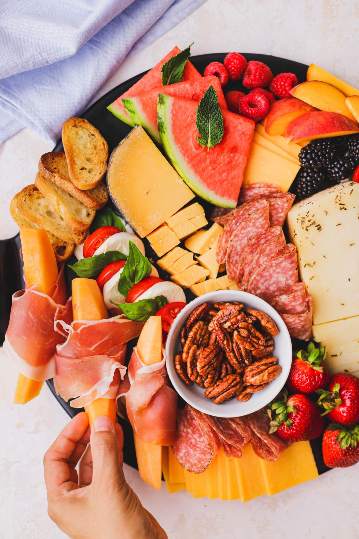 Sliced cantaloupe wrapped in prosciutto and served with a variety of fruits and crackers.