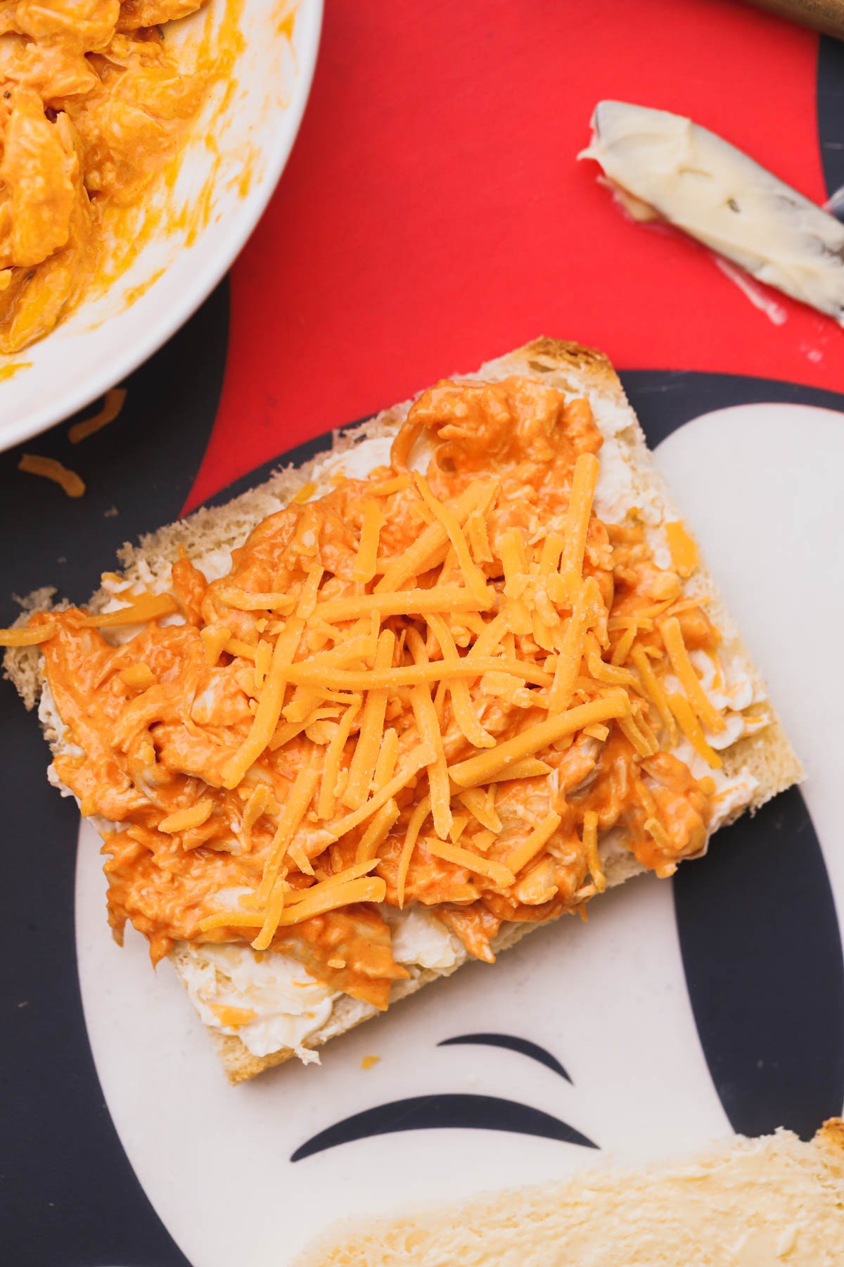 Sliced bread with cheese spread, spicy chicken and topped with extra cheddar cheese.  