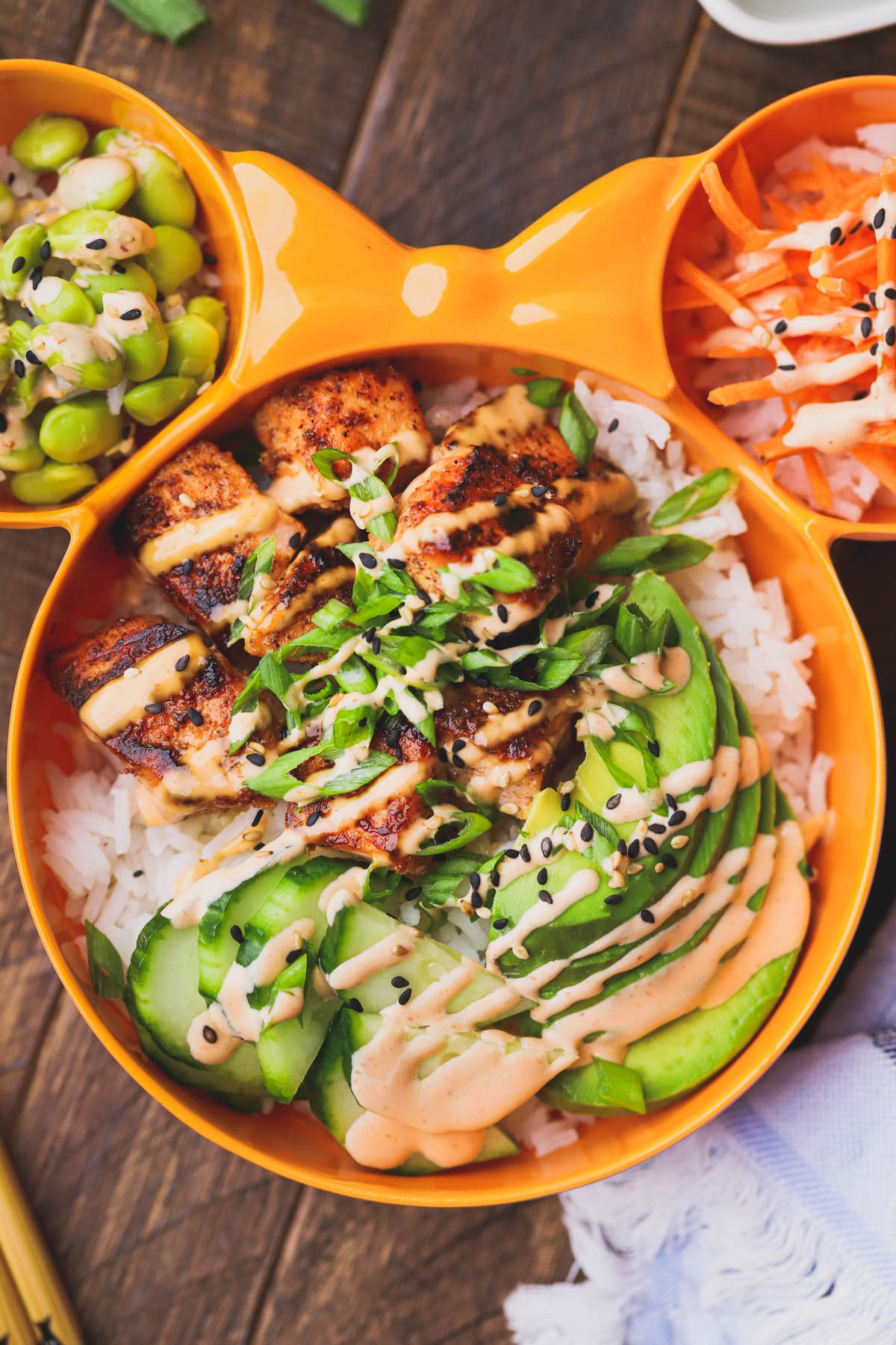 Spicy salmon bowl with crispy salmon, cucumbers, avocado, edamame, carrots, spicy mayo, scallions and sesame seeds.