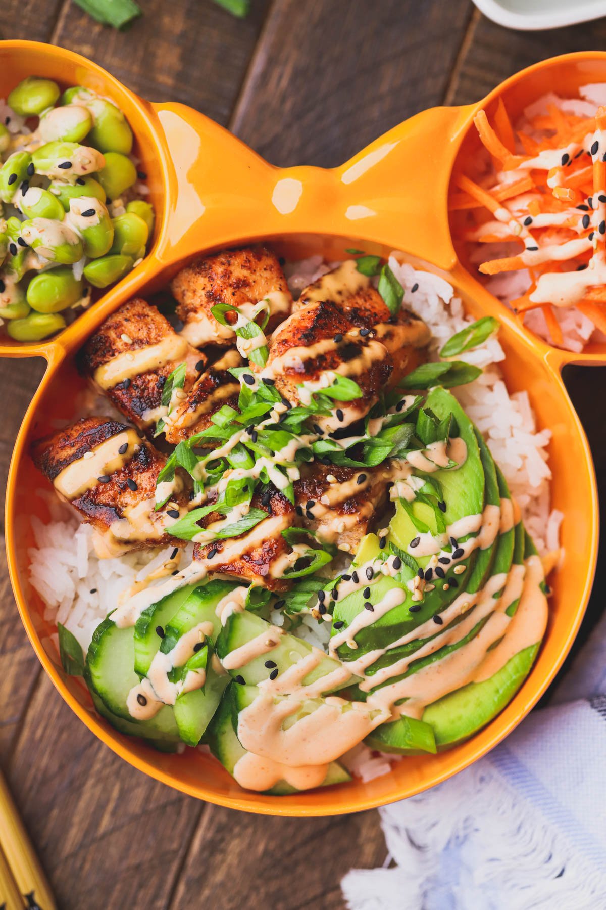 Spicy salmon bowl with crispy salmon, cucumbers, avocado,  edamame, carrots, spicy mayo, scallions and sesame seeds.