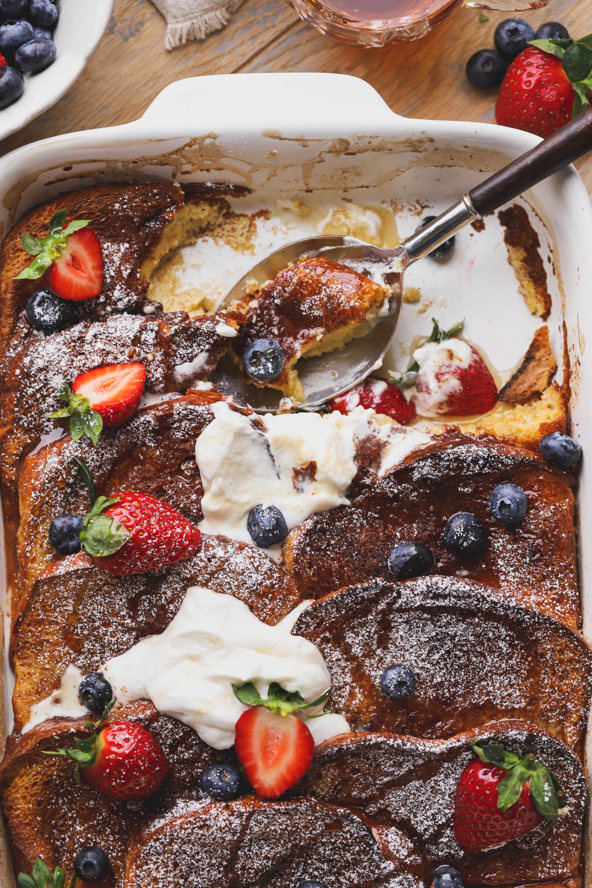 Baked brioche French toast bake with maple syrup, berries and powdered sugar.  