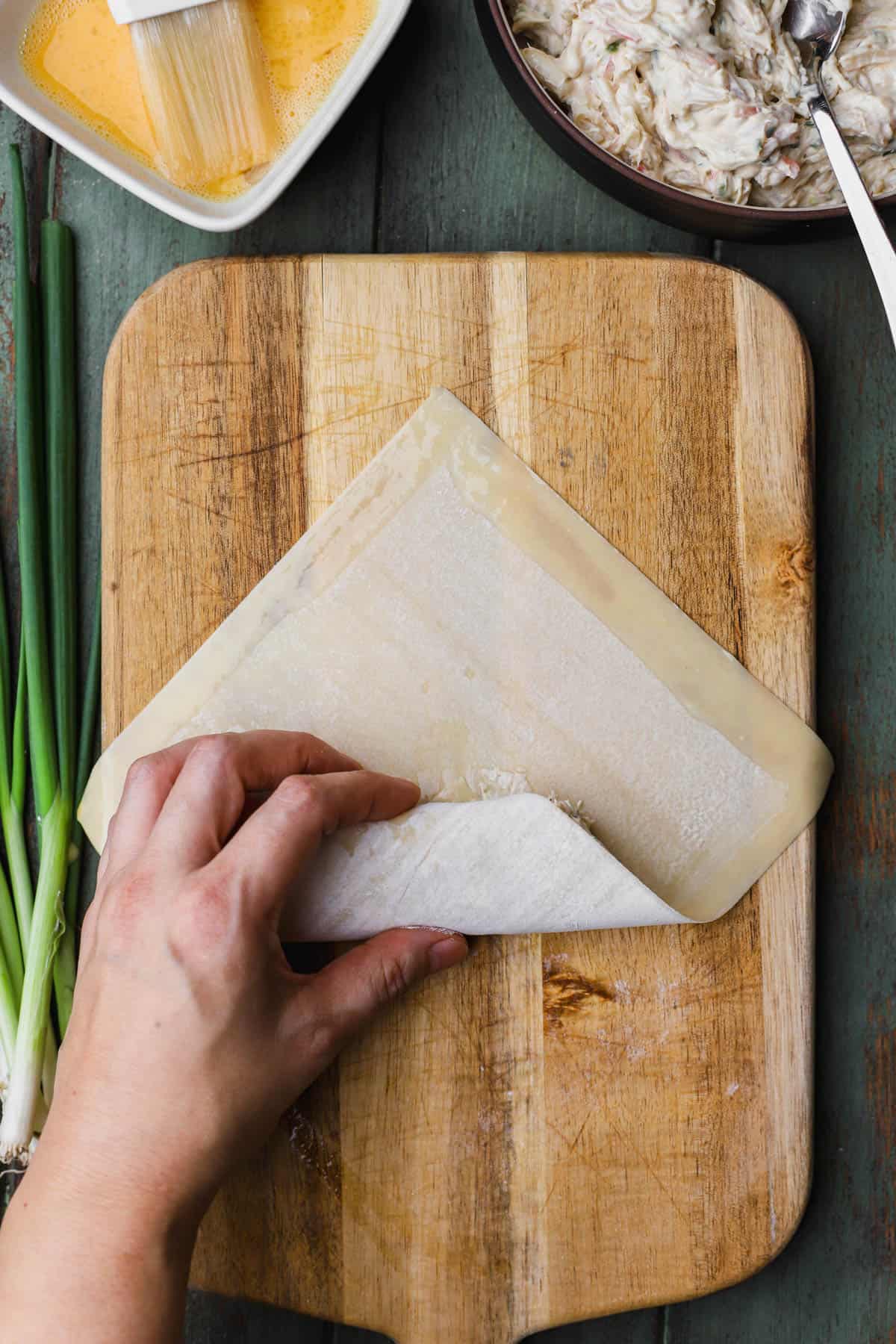 Folding over egg roll wrapper over filling. 