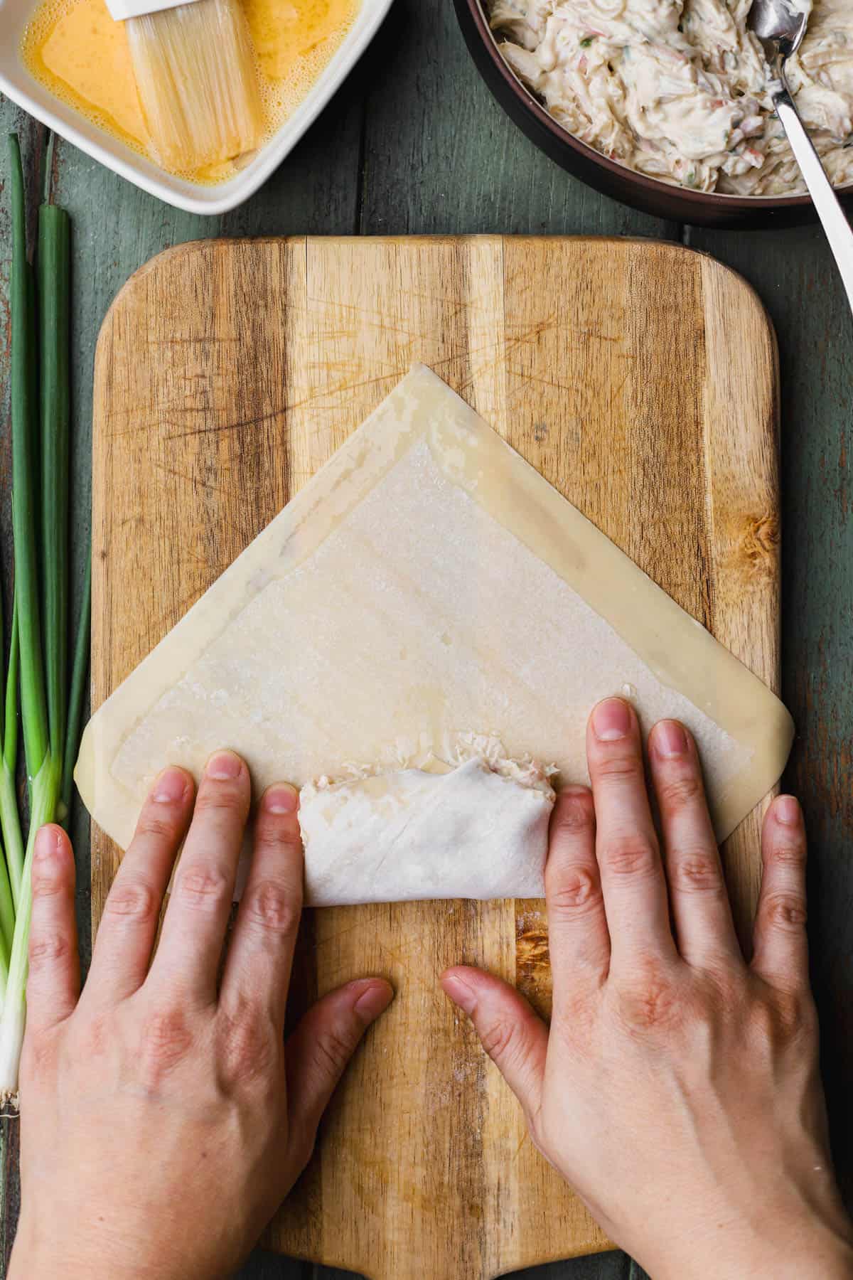 Flattening sides of egg roll wrapper. 