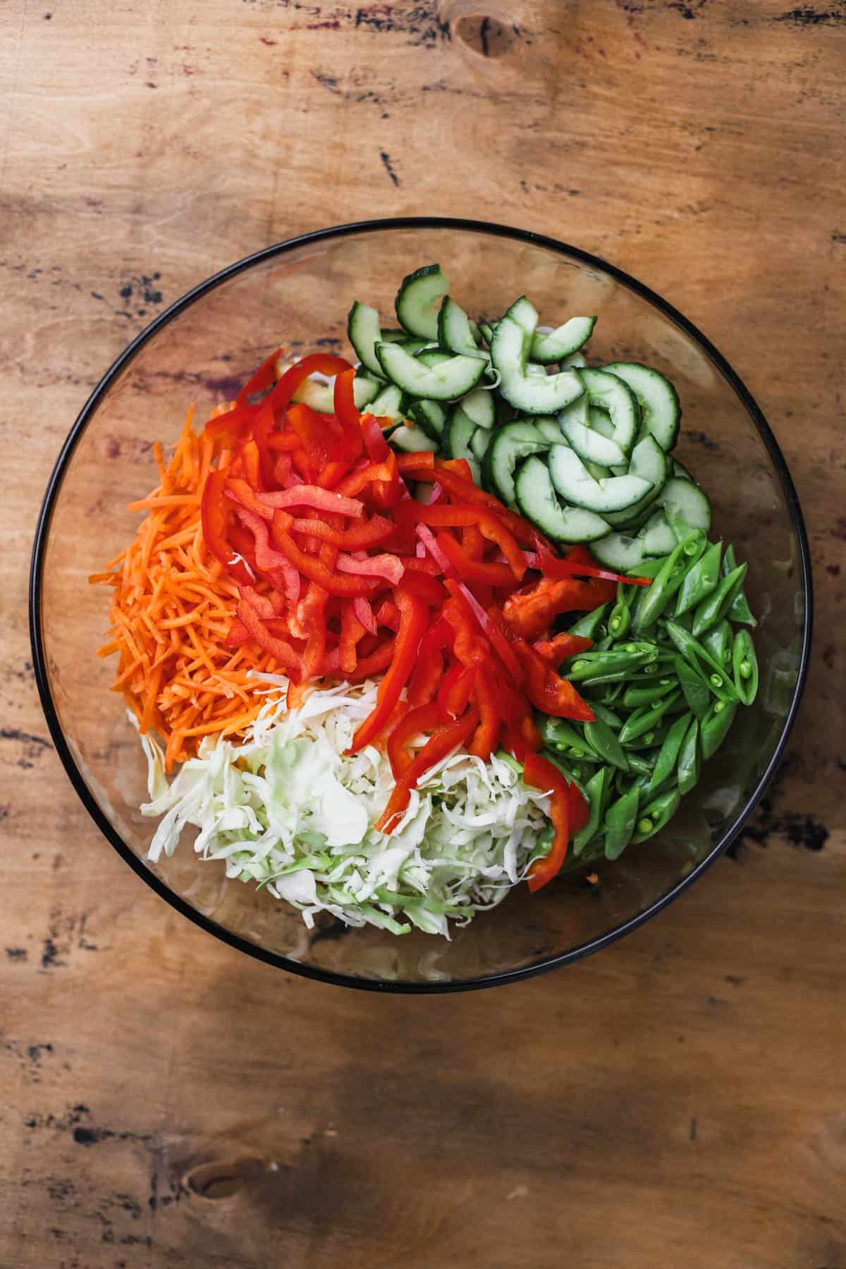 Rice noodles, carrots, red bell peppers, cucumber, shredded green cabbage, and sugar snap peas. 