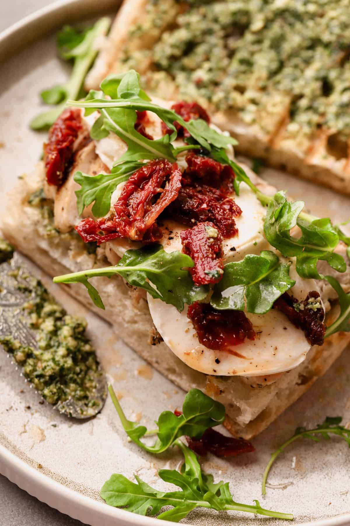 Sun-dried tomato pesto chicken sandwich with herb focaccia, fresh mozzarella slices, and fresh arugula.