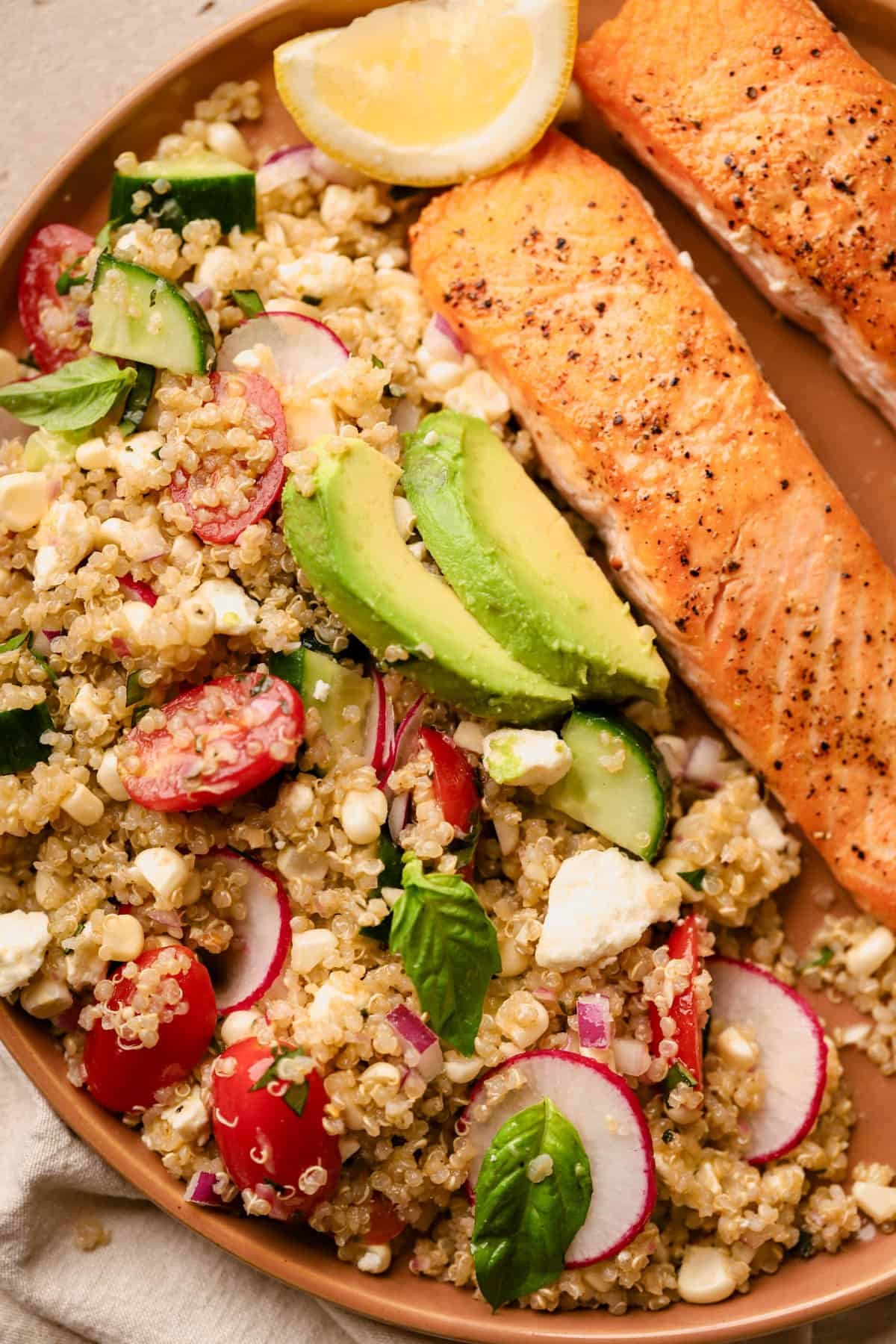 Quinoa salad with salmon is made with cucumbers, feta, cherry tomatoes, radishes, red onions, basil, avocado, and tarragon vinaigrette. 
