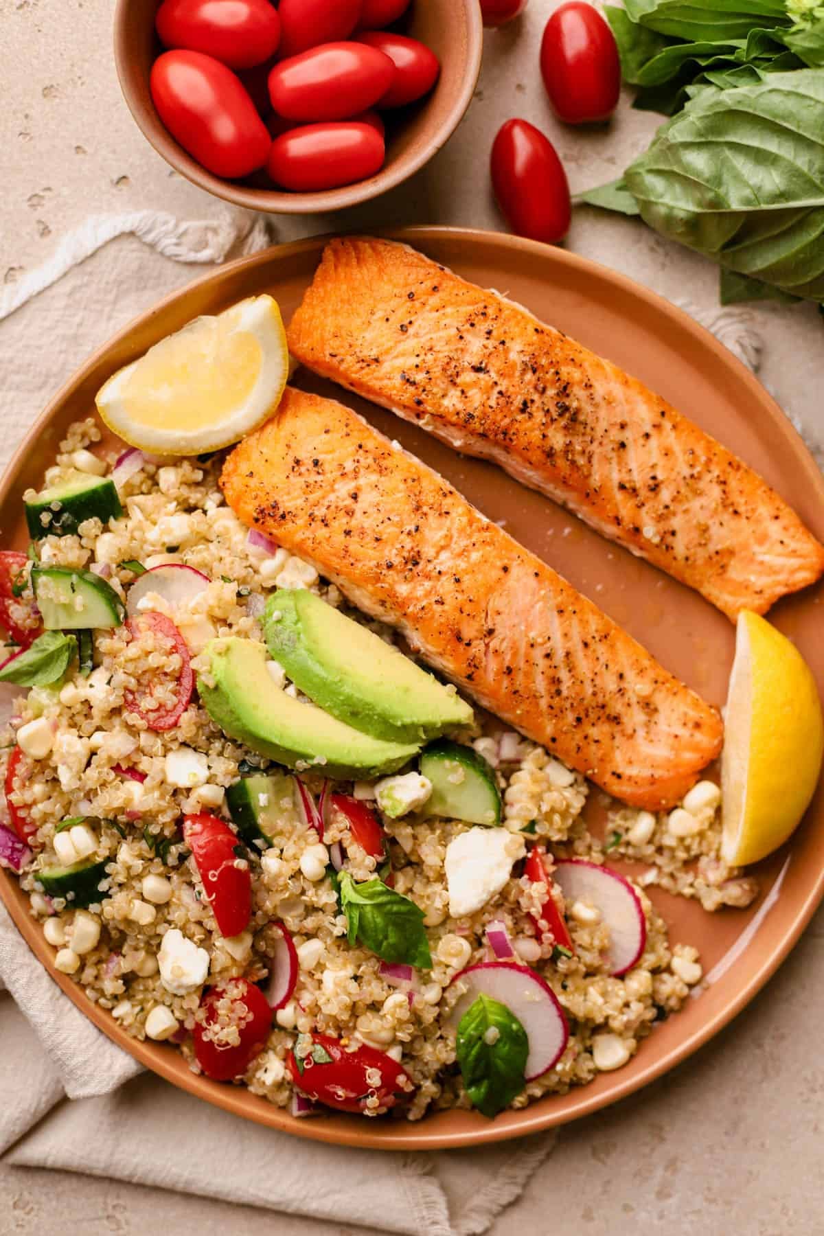 Quinoa salad with salmon is made with cucumbers, feta, cherry tomatoes, radishes, red onions, basil, avocado, and tarragon vinaigrette. 