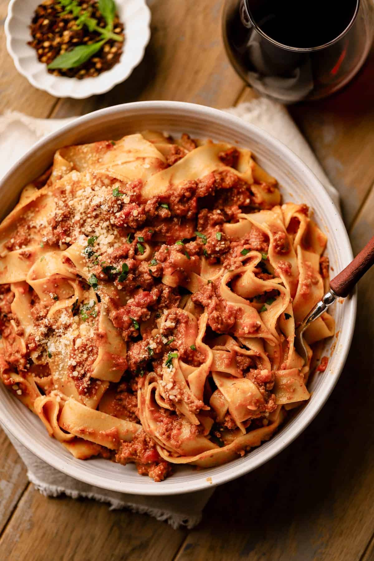 Spicy bolognese with pappardelle is made with ground beef, pancetta, spicy Italian sausage, red pepper flakes, fresh herbs, vegetables, tomatoes and red wine.  Served with pappardelle pasta and parmesan cheese.