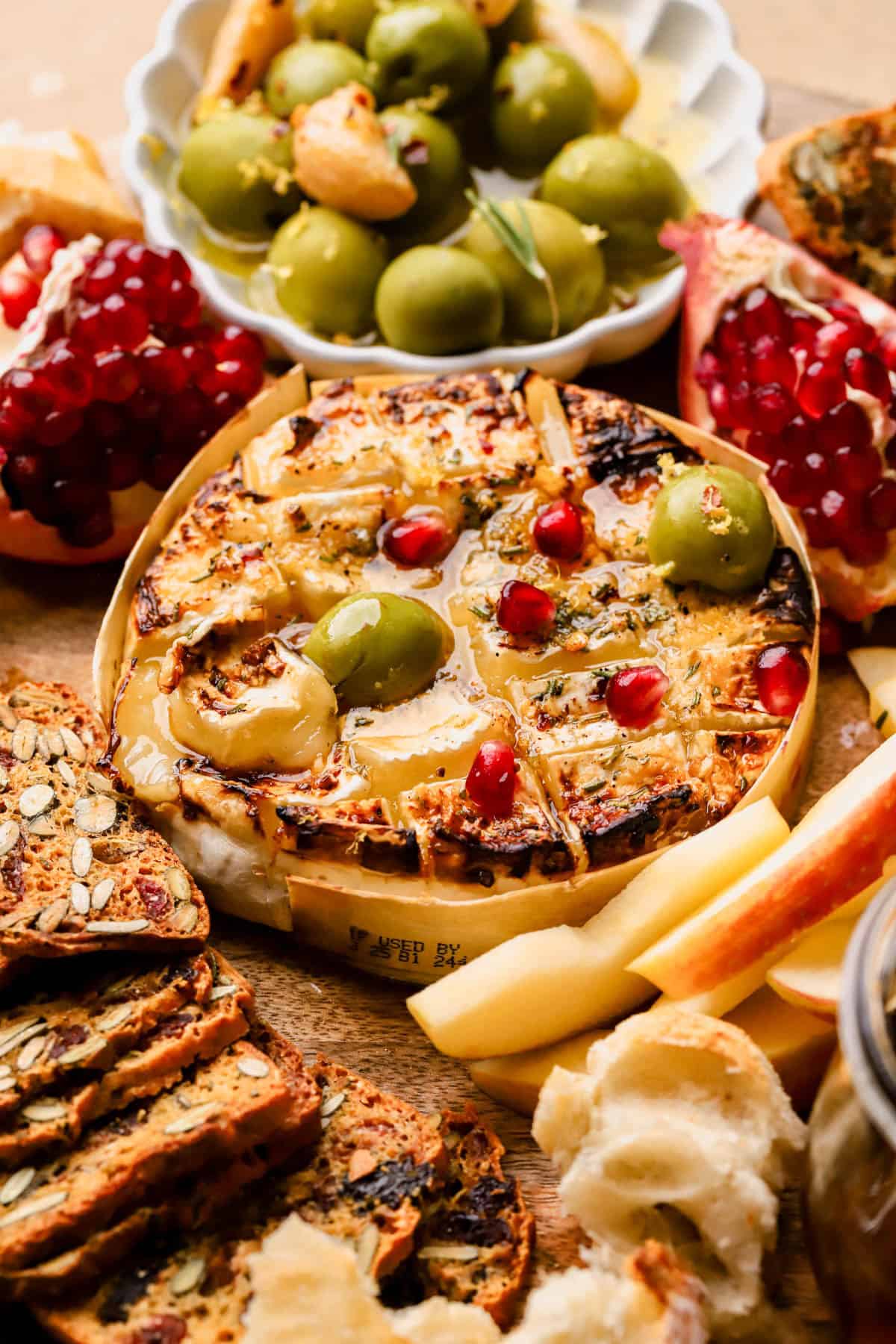 Brie cheese with honey, rosemary, and served with olives, pomegranates, crackers, and apples. 