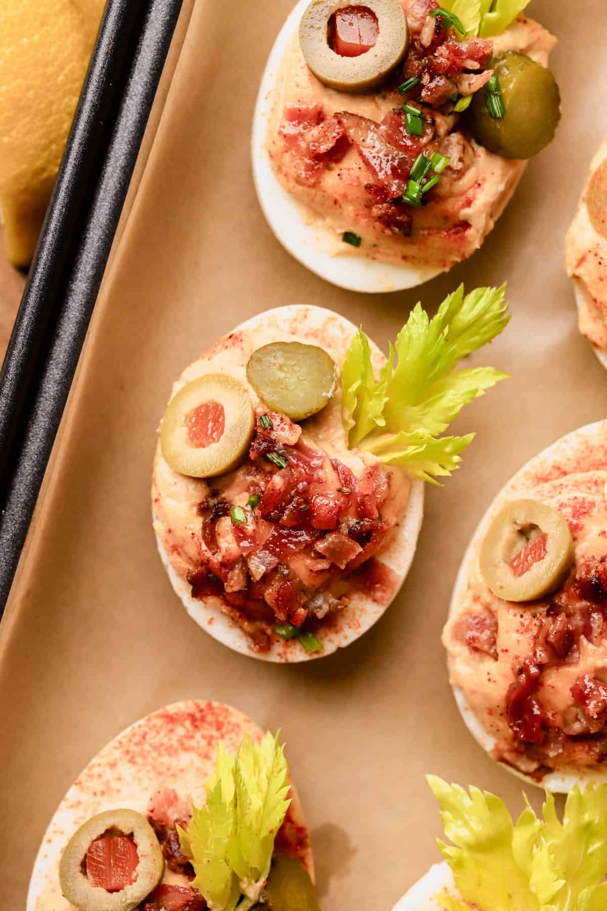 Bloody Mary Deviled Eggs are made with tomato paste, horseradish, dijon, celery seed, Tabasco, and topped with bacon, olives, celery leaves, chives, and gherkins.