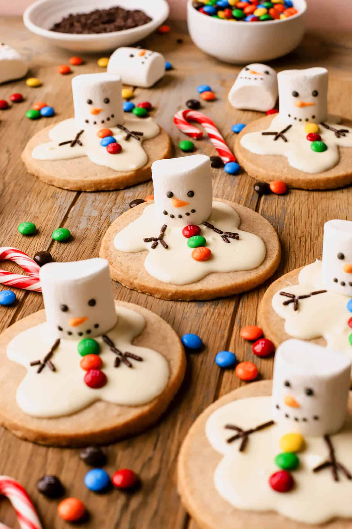 Cinnamon shortbread cookies decorated as melty snowmen, with white chocolate, decorated Jet-Puffed marshmallows, mini M&M's and chocolate jimmies.