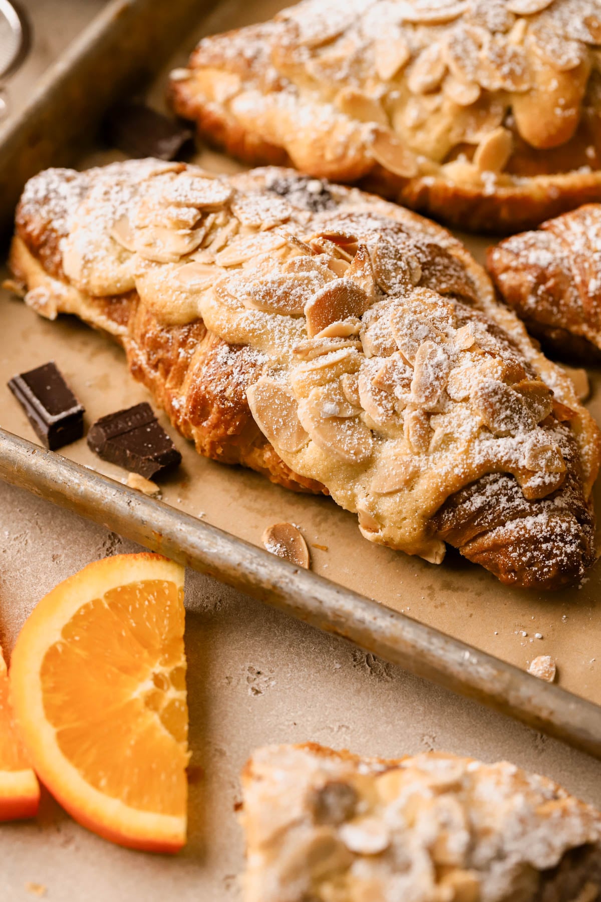 Side view of chocolate almond croissant with sliced almonds and powdered sugar. 