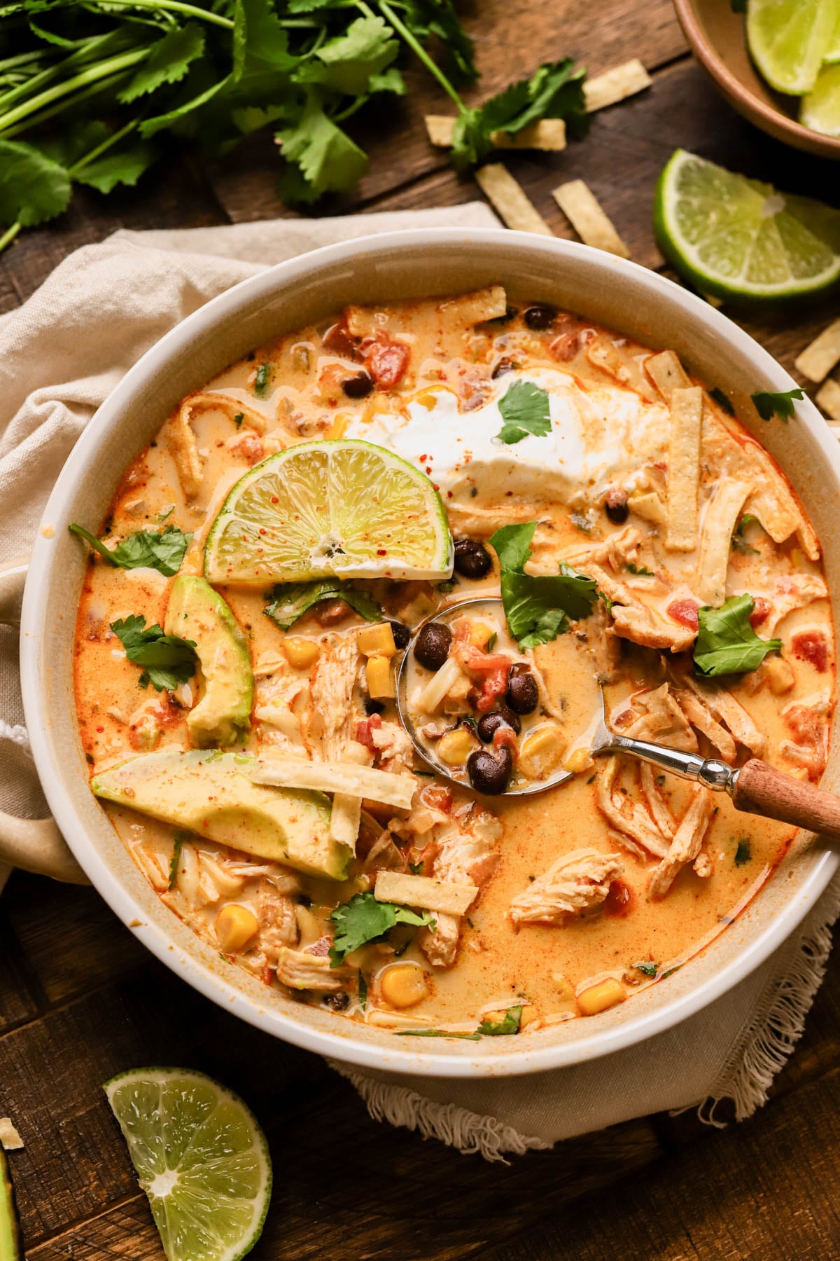Creamy chicken taco soup is made with shredded chicken, black beans, Rotel tomatoes, corn, onions, garlic, and cream cheese.  Topped with avocado, cheese, cilantro, sour cream and lime.