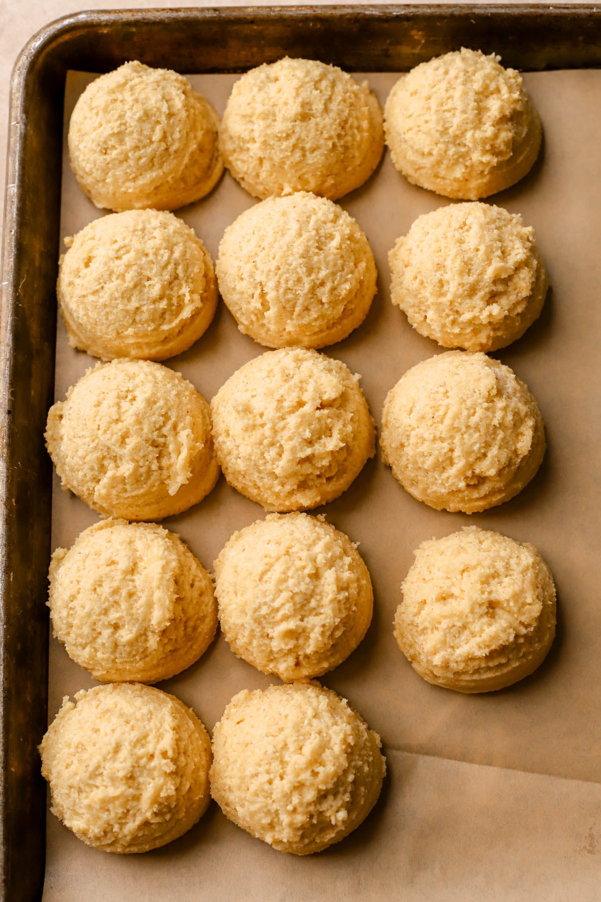 Scooped cornmeal cookies on parchment lined baking sheet. 