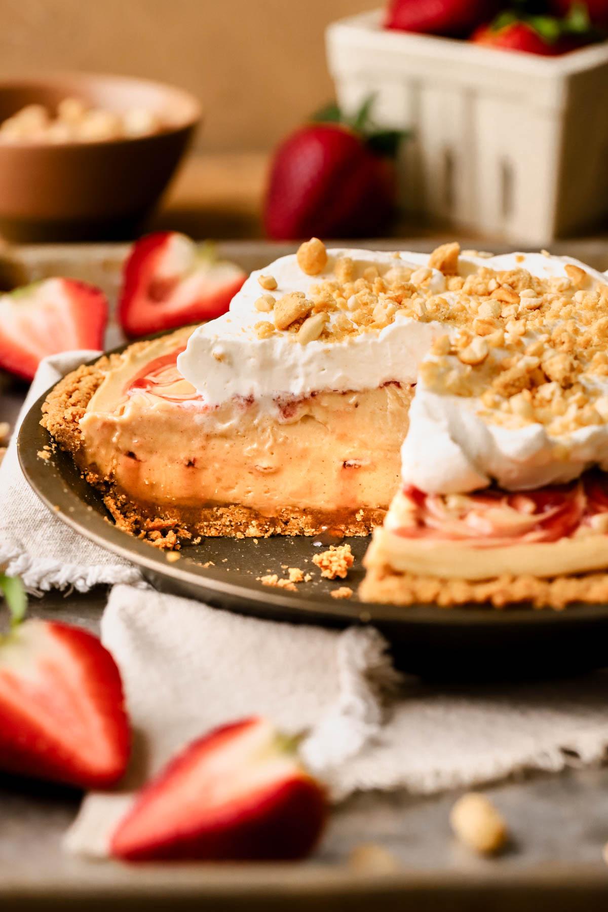 Side view of sliced peanut butter and jelly pie, with peanut butter mousse filling, swirls of strawberry jam, homemade whipped cream, peanuts, and crushed Nutter Butter cookies. 