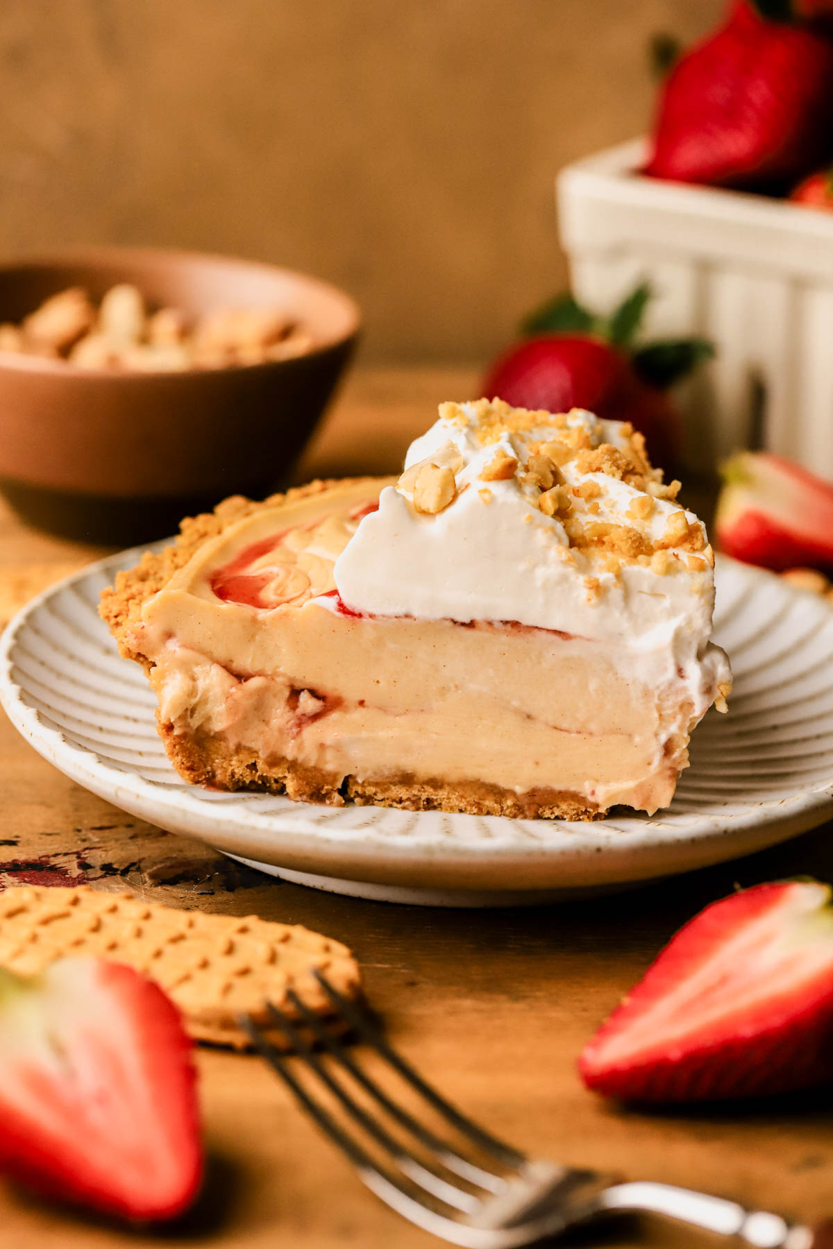 Close up of sliced peanut butter and jelly pie with a Nutter Butter cookie crust, peanuts, whipped cream, and strawberry jam. 