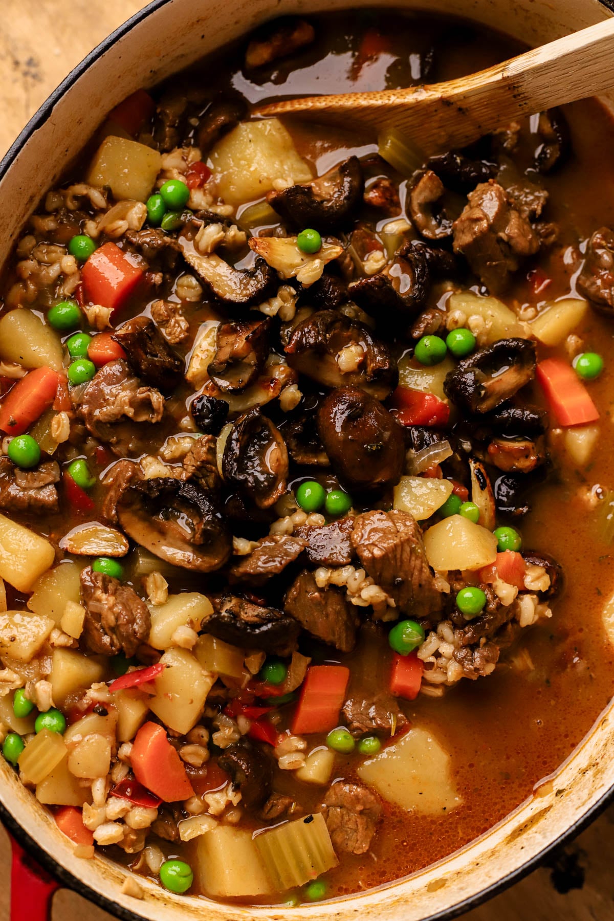 Close up of beef barley mushroom soup with veggies, peas, and gold potatoes. 